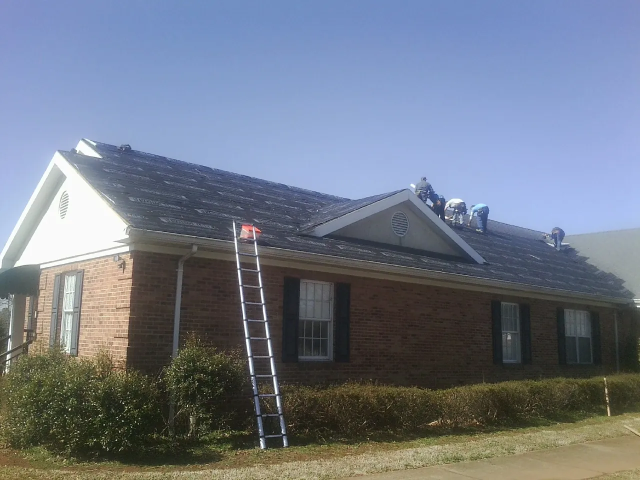 Crew tearing shingles off a brick ranch roof with a ladder set — Emergency Roof Repair work by our crew in Pikesville