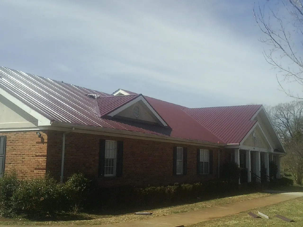 Red metal roof with gabled entries on a long brick building, from a Hail Damage Roof Repair job in Pikesville