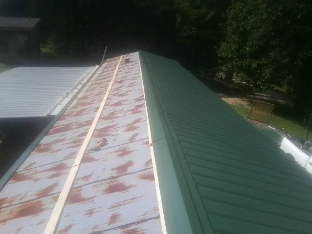 Old rusted panels beside newly installed green metal roofing — Wind Damage Roof Repair by Roofing Brothers in Pikesville