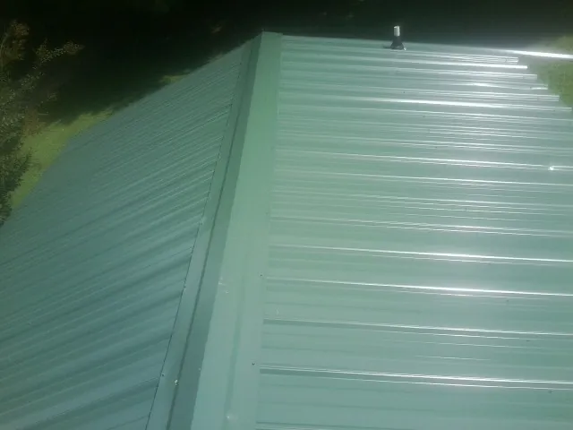 New green metal panels meeting at the ridge of a roof — Flat Roof Repair work by our crew in Pikesville