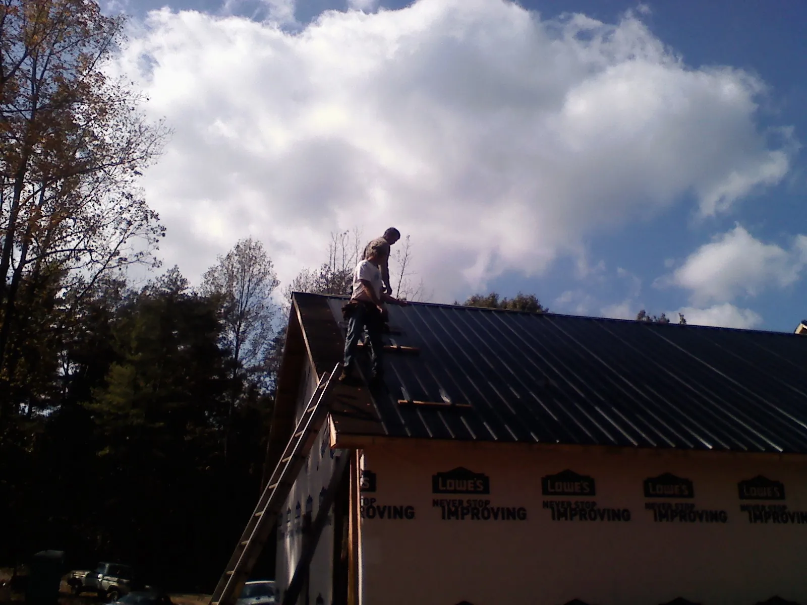 Roofer fastening dark metal panels high against a cloudy sky, from a Roof Inspection job in Pikesville