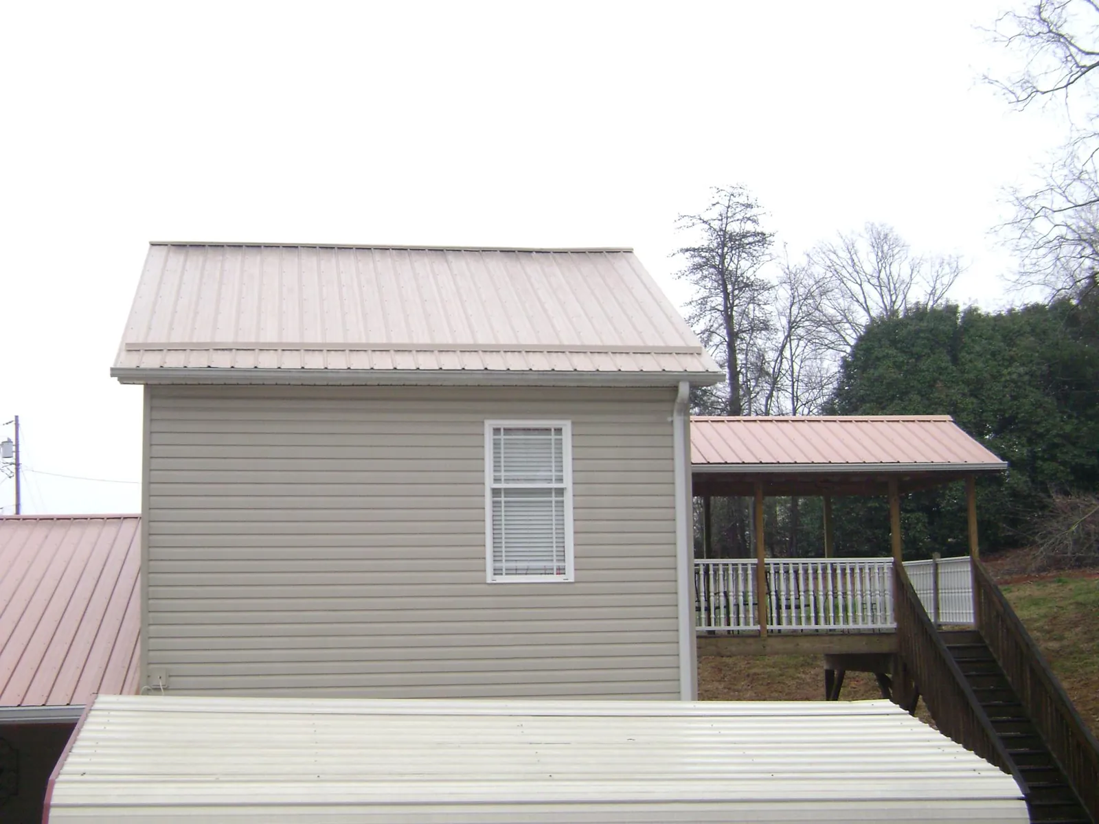 Tan metal roofs on a two story addition and attached porch, from a Roof Replacement job in Pikesville